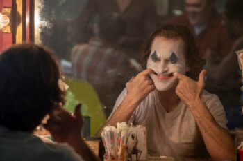 Arthur Fleck (Joaquin Phoenix) se force à sourire, maquillé en clown